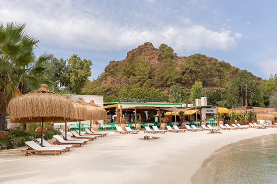 A view of Manos Beach at D Maris Bay resort. Sun loungers sit in pairs on the beach, while Manos fish restaurant is in the background