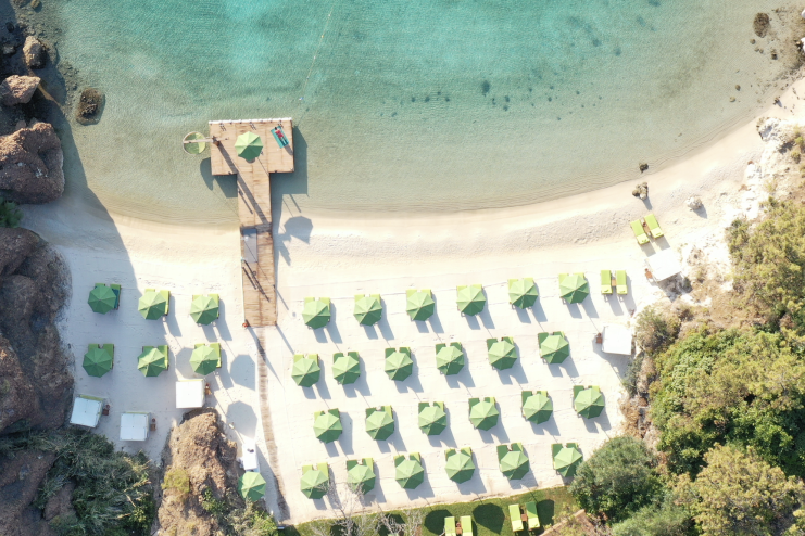 A birdseye view of the white sand and bright blue sea of Silence Beach at D Maris Bay resort, with a wooden jetty and rows of sunbeds on which to relax on.